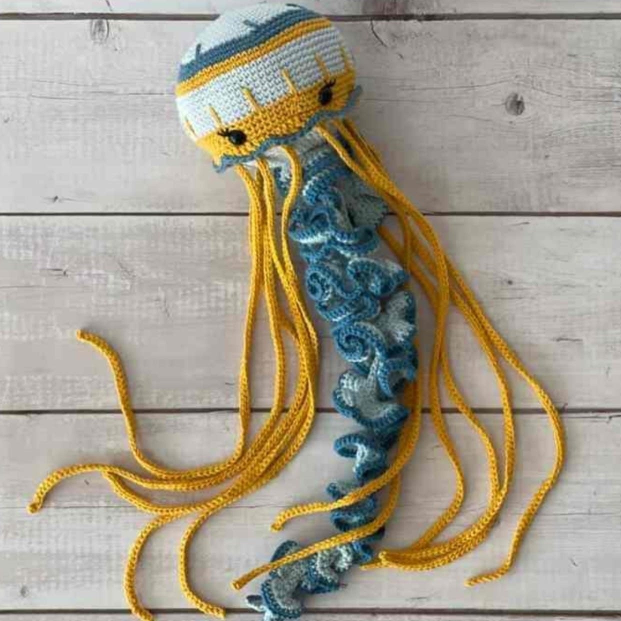 Crochet jellyfish with a blue and yellow tail, showcasing its colorful and handmade design.