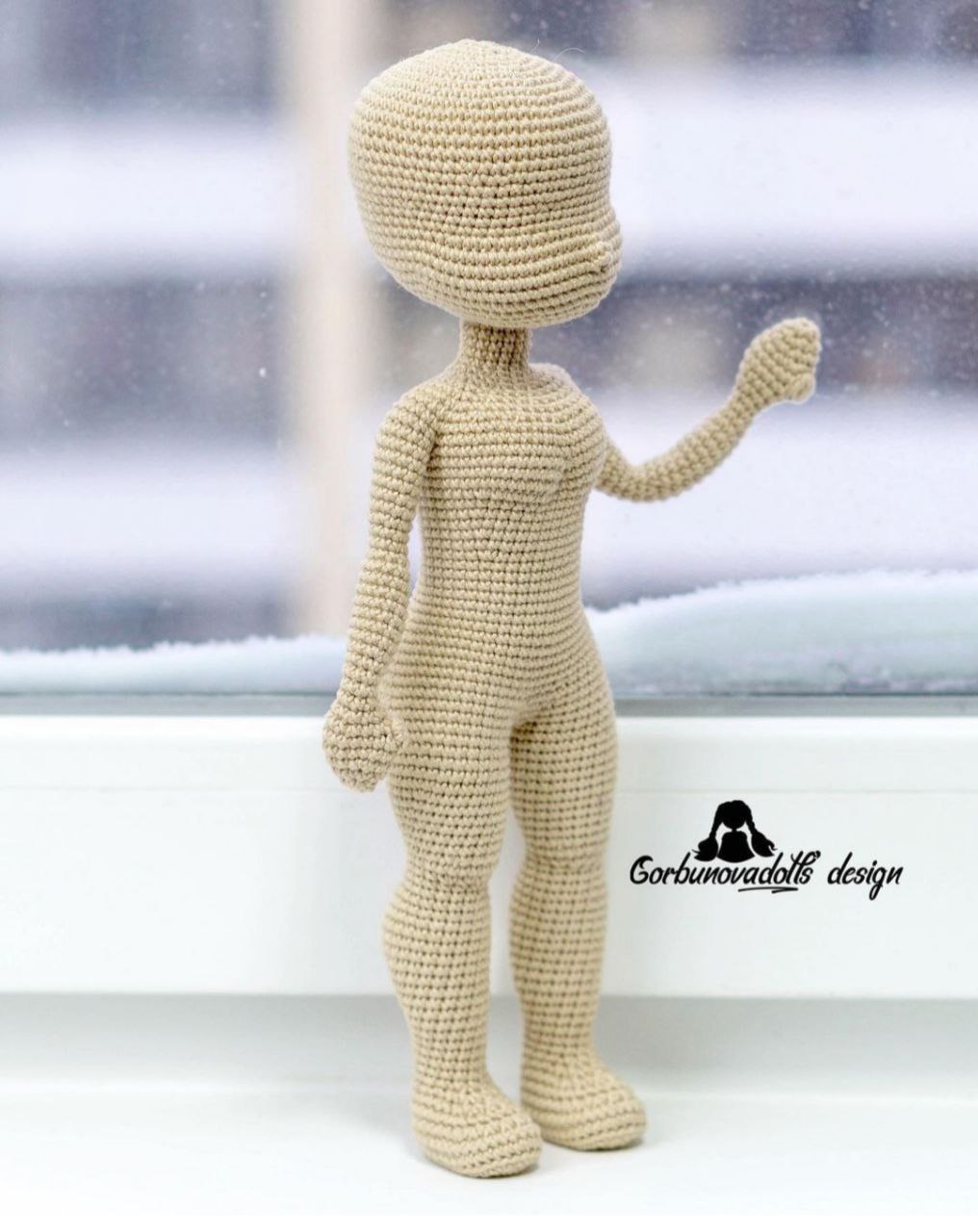 Crochet doll base figure standing in front of a window, highlighting its colorful design and handmade details.