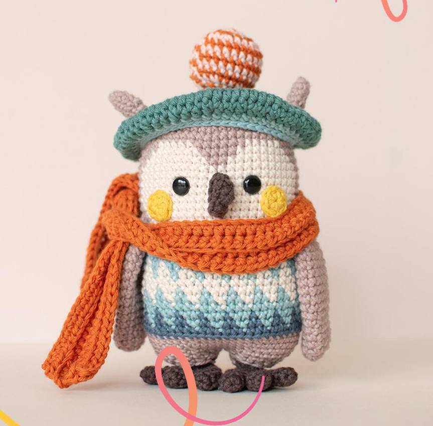 Crochet owl with a hat and scarf, featuring a colorful and cozy design against a neutral background