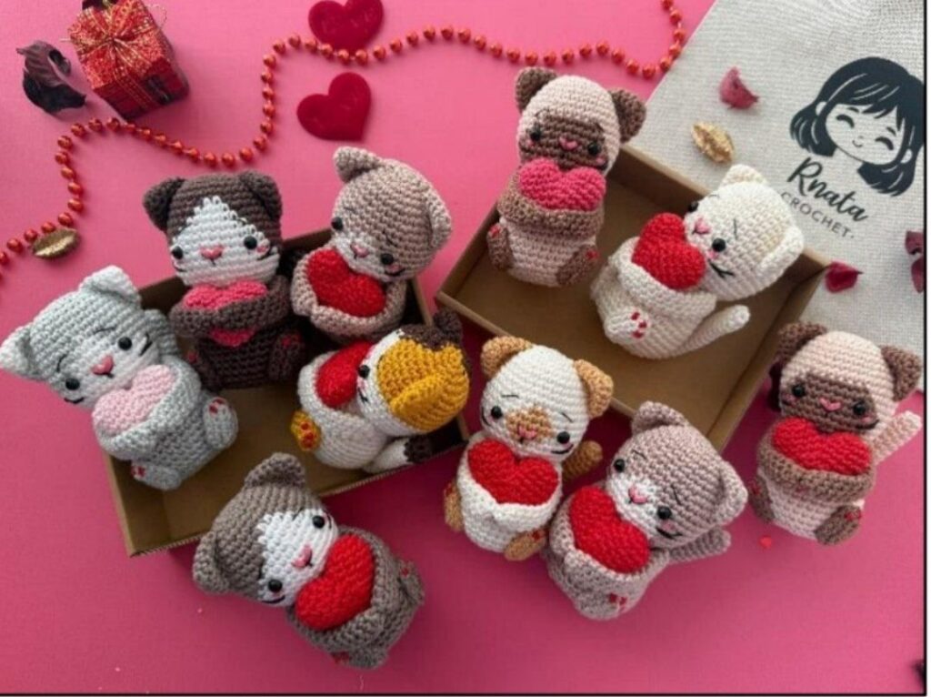 Several crocheted cat figures with hearts, carefully arranged in a box, highlighting their creativity and detail for Valentine's Day.