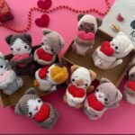 Several crocheted cat figures with hearts, carefully arranged in a box, highlighting their creativity and detail for Valentine's Day.