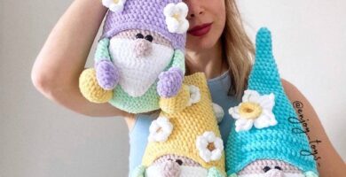 Handmade pastel crochet gnomes with decorative flowers, held by a woman wearing a daisy headband. Artisan amigurumi dolls woven with soft yarn.