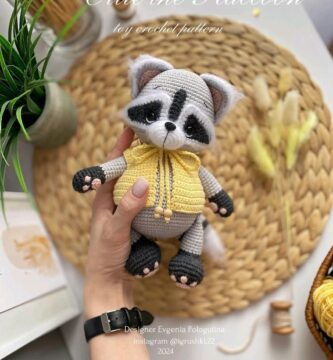 Raccoon with a yellow sweater, entirely crocheted, displaying a curious and playful expression.