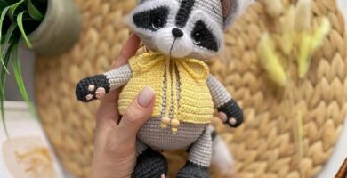 Raccoon with a yellow sweater, entirely crocheted, displaying a curious and playful expression.